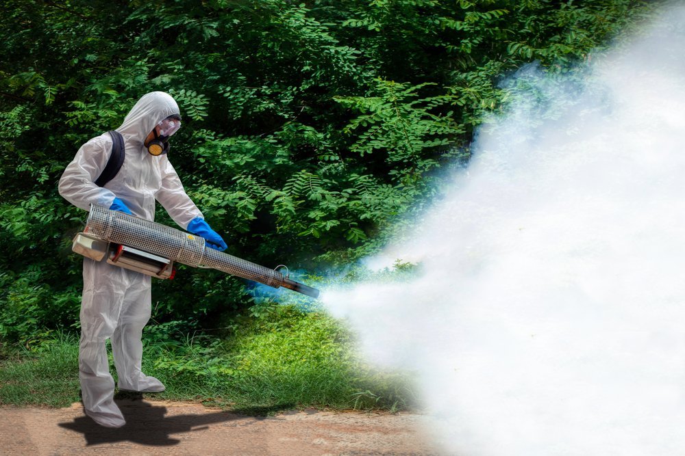 man in a white suit spraying for bugs outside
