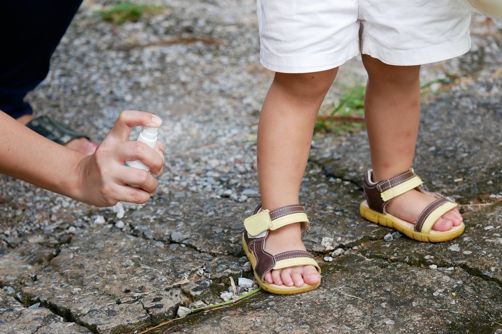 someone spraying a child's feet with bug spray