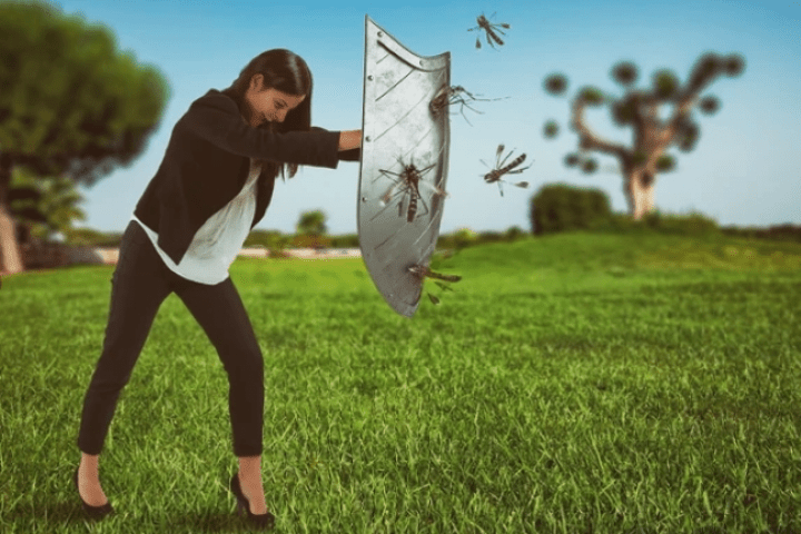 woman in business clothes holding a shield against mosquitos while on a lawn
