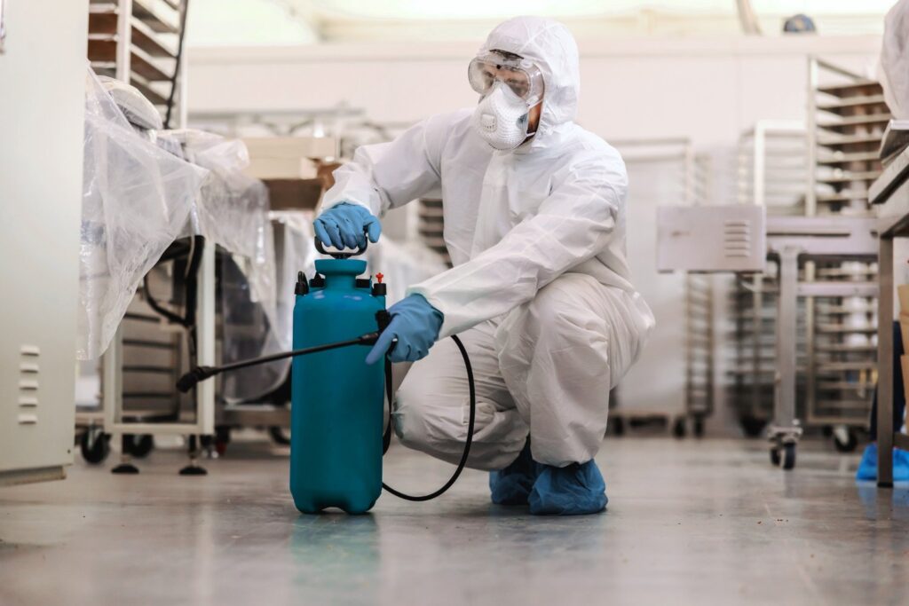 exterminator in white suit spraying a cafeteria for insects and rodents